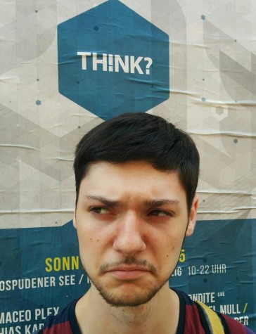 Alex Wilson takes a selfie while traveling Germany. Alex is, ironically, lost in his thoughts while standing in front of a poster that says, “TH!NK?”