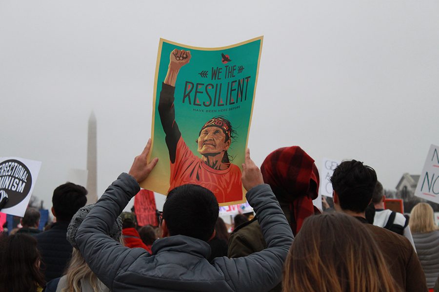 With the Washington Monument in the background, a man holds one of the signs distributed by the Amplifier Foundation. The sign, reading “We the resilient have been here before,” was created by artist Ernesto Yerena. 
