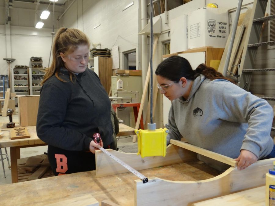 In+the+beginning+stages+of+a+woodworking+project%2C+senior+Bethany+Plennert+helps+senior+Tayler+Varner+make+measurements+on+parts+of+her+chair%2C+that+is+designed+to+look+like+the+lower+peninsula+of+Michigan+