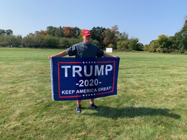 Showing off his flag in front of Stockbridge High School’s apple orchard, Drew Davis 12 represents who he wants to win the 2020 presidential election. Davis thinks that Donald Trump is the best fit for the presidency for the next four years. 