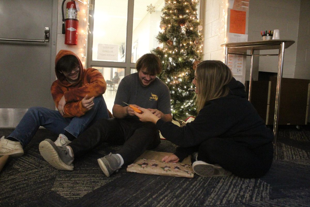 Preparing for the holiday season, juniors Christian Anthony and Nick Graves help senior Azora Parks wrap up Christmas gifts.